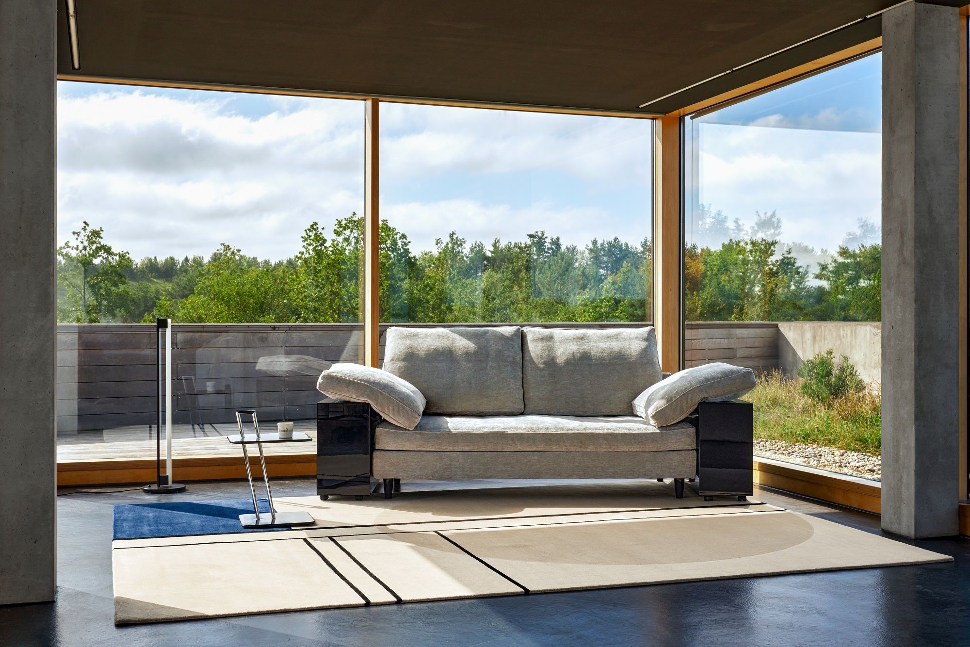 Graues Lota Sofa von Classicon in modernem Wohnzimmer mit großem Fenster und Teppich.
