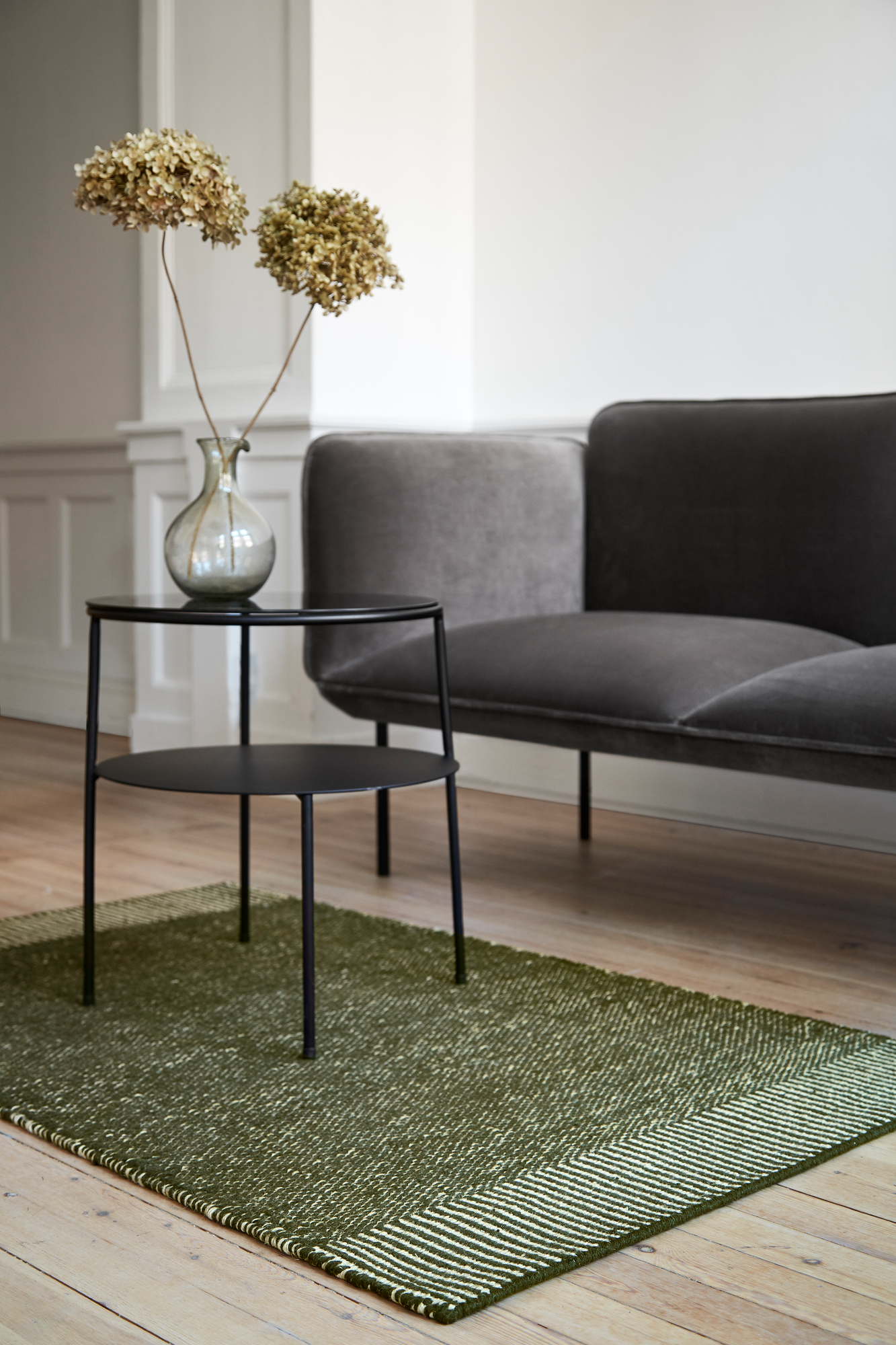 Eleganter Duo Beistelltisch Schwarz von Woud mit dunklem Rauchglas neben einem grauen Sofa.