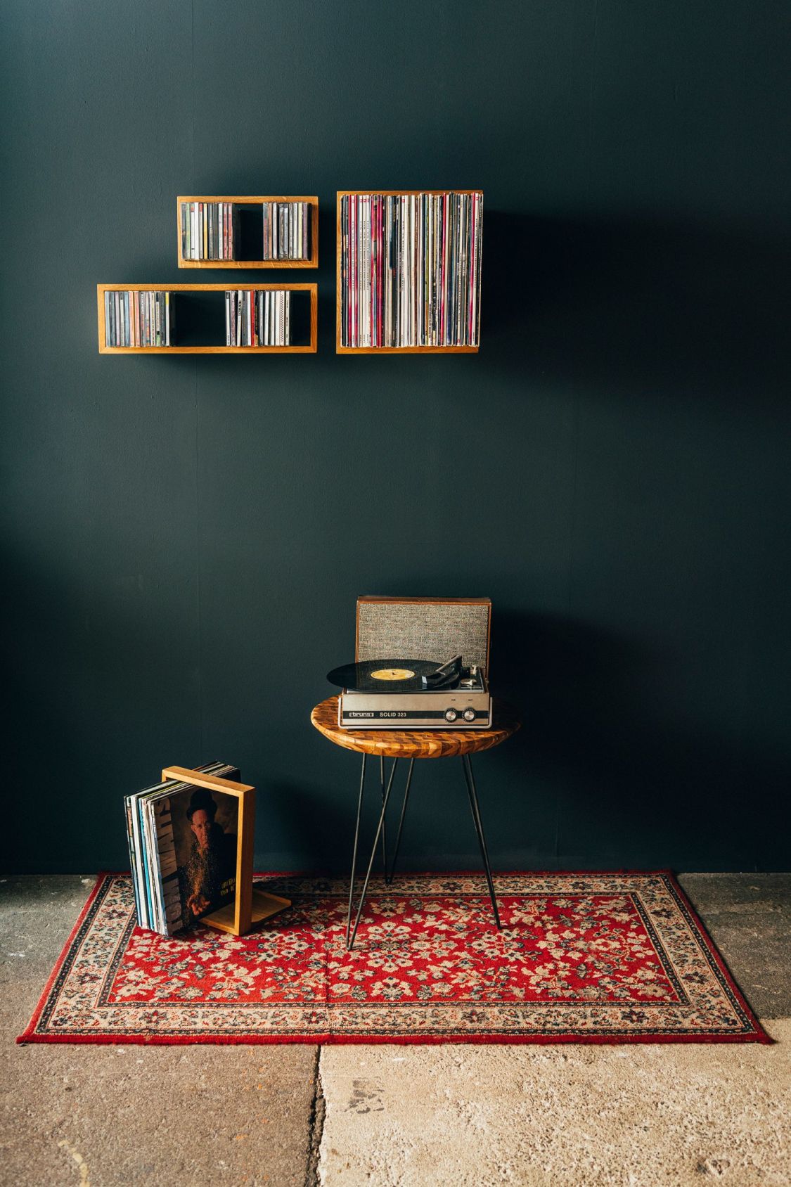 Vintage Interieur mit Schallplattenspieler auf Tisch, Schallplattenregalen und rotem Teppich vor dunkler Wand.