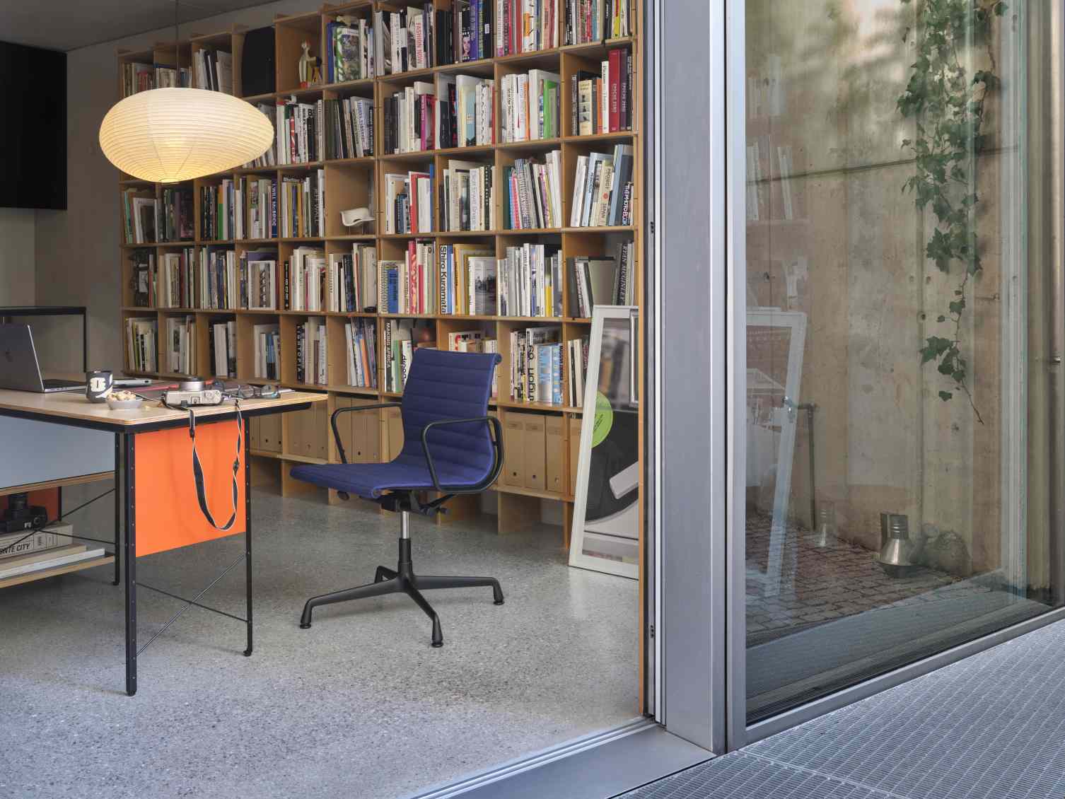 Blauer Vitra Aluminium Chair EA 132 Bürostuhl im modernen Arbeitszimmer mit Bücherregal.