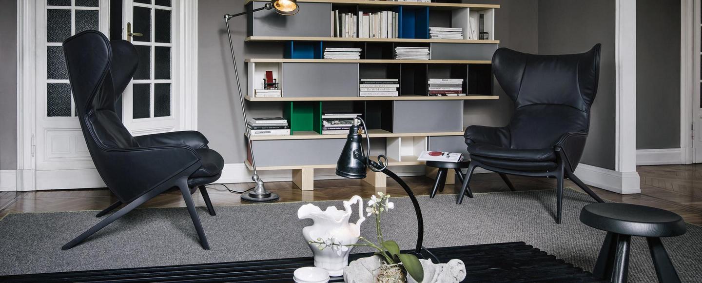 Schwarzer Cassina Sessel mit hoher Rückenlehne und passendem Hocker in modernem Wohnzimmer.