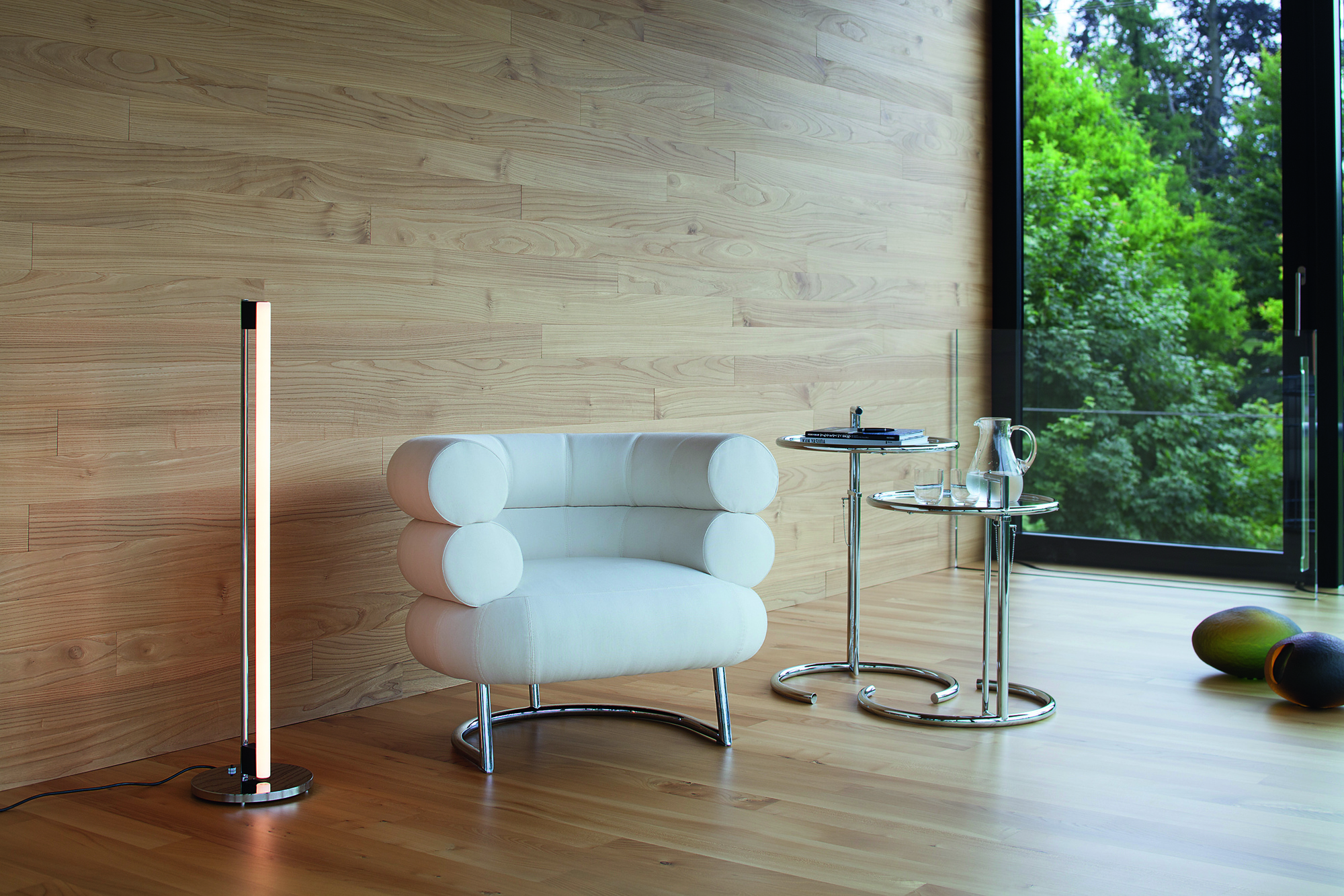 Moderner Wohnraum mit ClassiCon E1027 Beistelltisch, verstellbar, neben Sessel und Stehlampe auf hellem Holzboden.