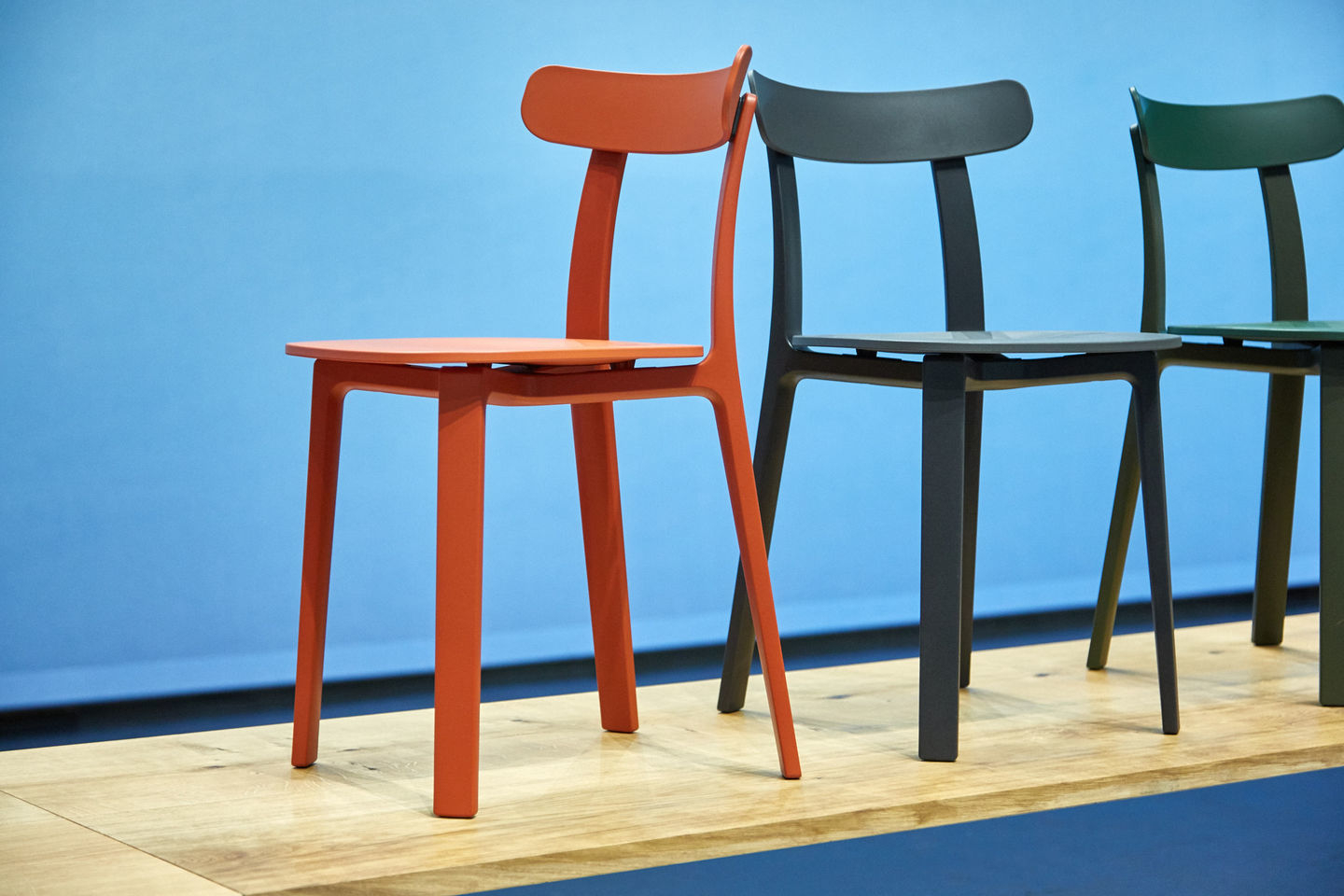 Vitra All Plastic Chair Outdoor Stuhl in Orange, Grau und Grün vor blauem Hintergrund.