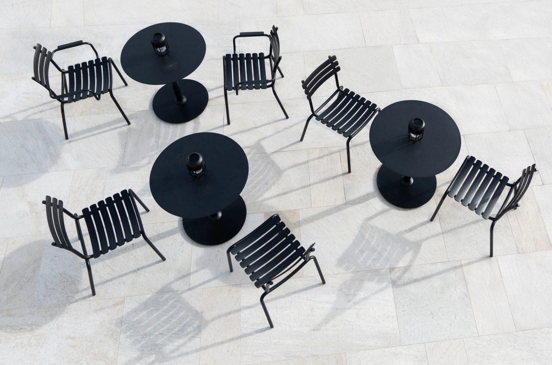 Draufsicht: Mehrere Alua Dining Stühle von Houe mit schwarzen Outdoor-Tischen auf heller Terrasse.