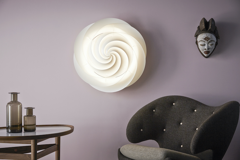 Weiße Swirl Deckenleuchte von Le Klint an lila Wand, spiralförmiges Design, moderne Beleuchtung.