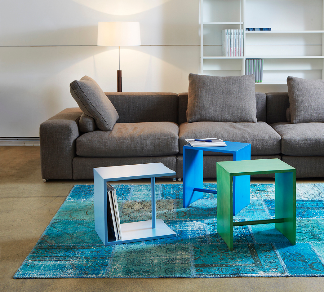 Ulmer Hocker Max Bill in Blau, Grün und Hellblau als Beistelltische vor grauem Sofa.