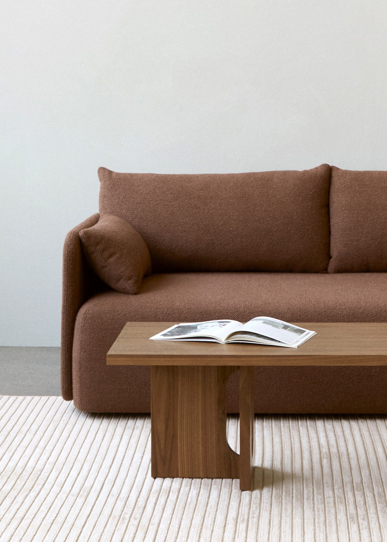 Offset Sofa von Audo Copenhagen, braunes 3-Sitzer Sofa mit Holztisch und offenem Buch im minimalistischen Wohnzimmer.