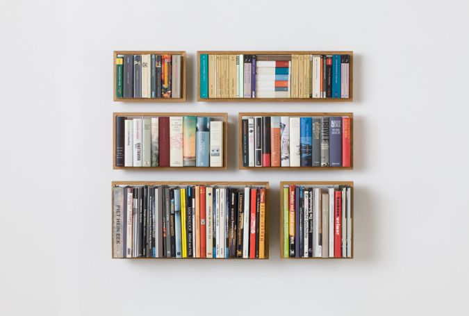 Sechs kleine, quadratische Regale aus Eiche, gefüllt mit Büchern, hängen an einer weißen Wand.