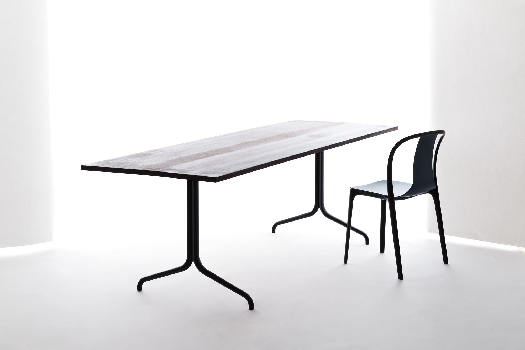 Vitra Belleville Chair Plastic Stuhl in Schwarz neben einem Esstisch mit dunkler Tischplatte.