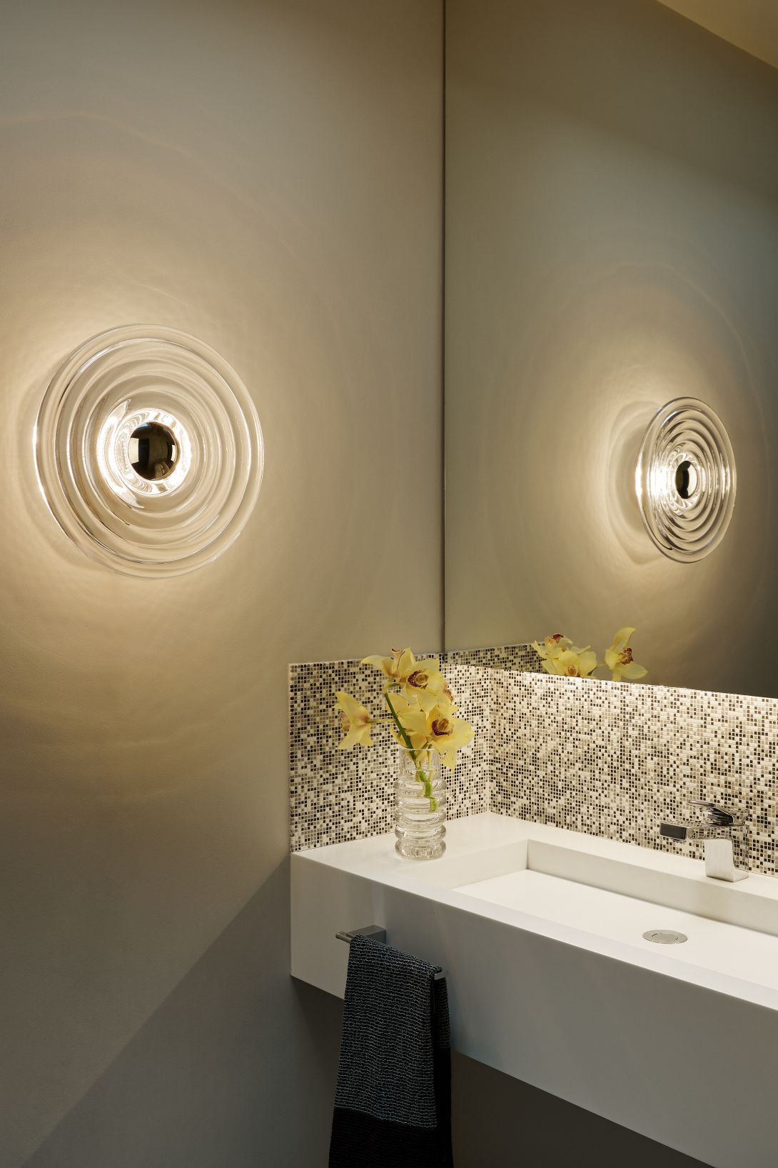 Tom Dixon Press Surface Large Wandleuchte aus Glas im Badezimmer mit Waschbecken und Spiegel.