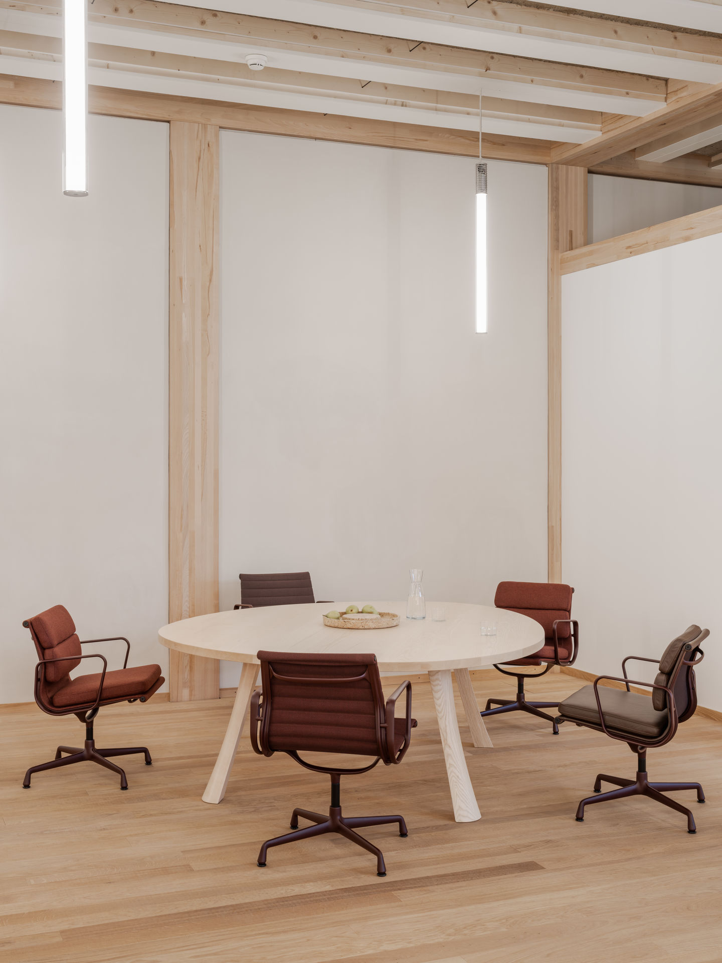 Vitra Aluminium Chair EA 108 in braun um einen hellen Holztisch in einem Besprechungsraum.