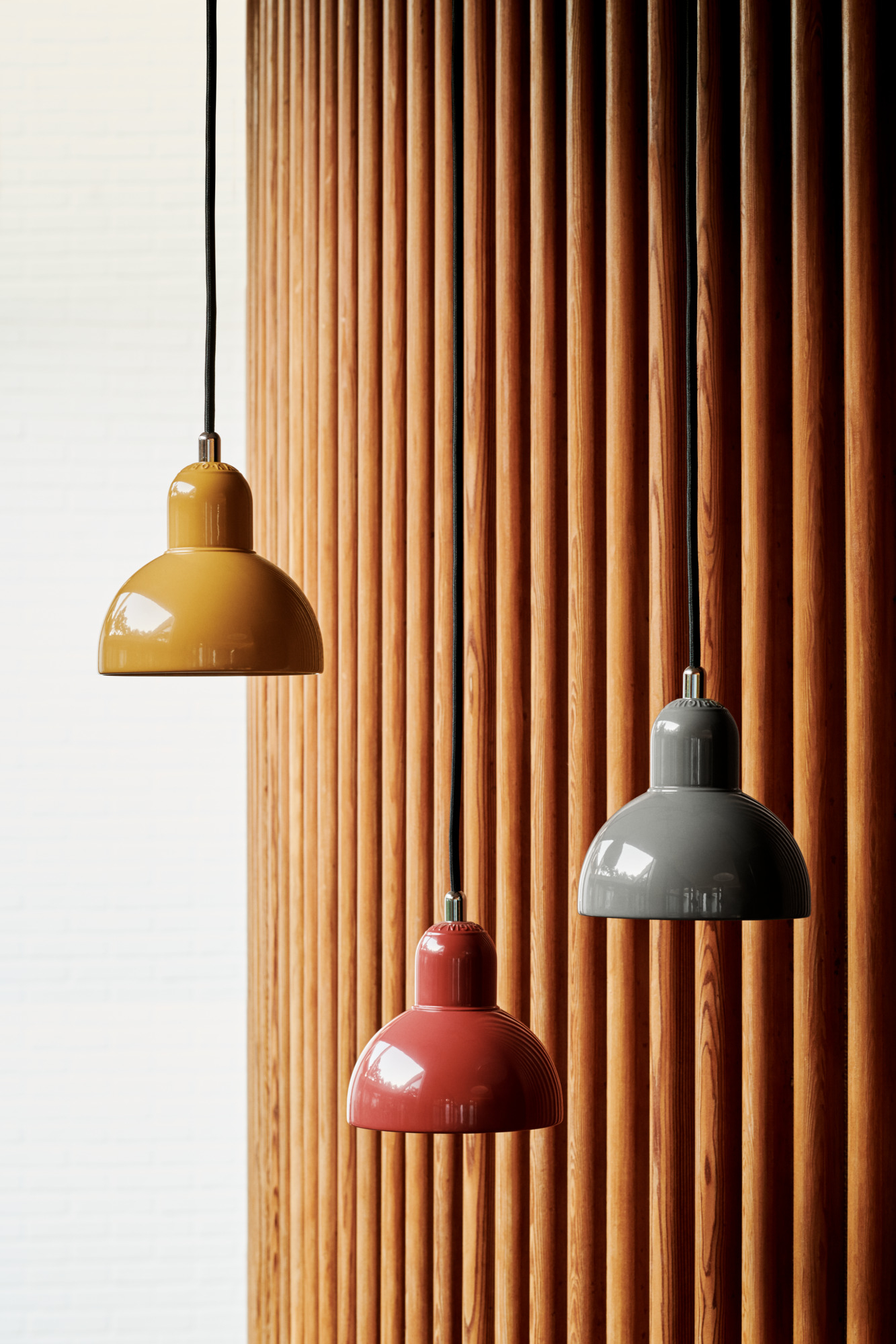 Drei Fritz Hansen Pendelleuchten 6722-P in Gelb, Rot und Grau vor Holzwand.