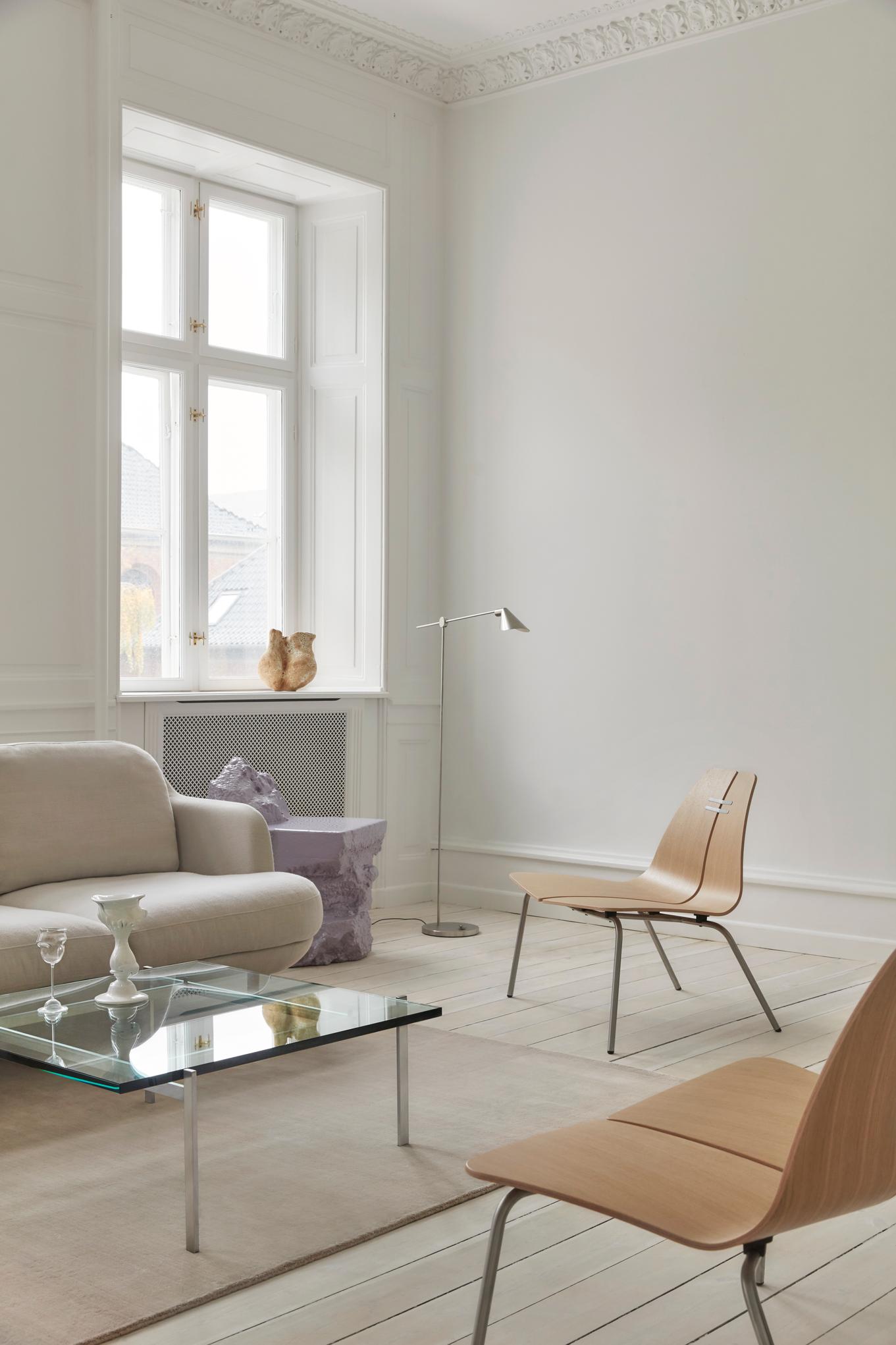 Heller Wohnraum mit Fritz Hansen PK23 Loungesessel aus Holz, Glascouchtisch und Designelementen.