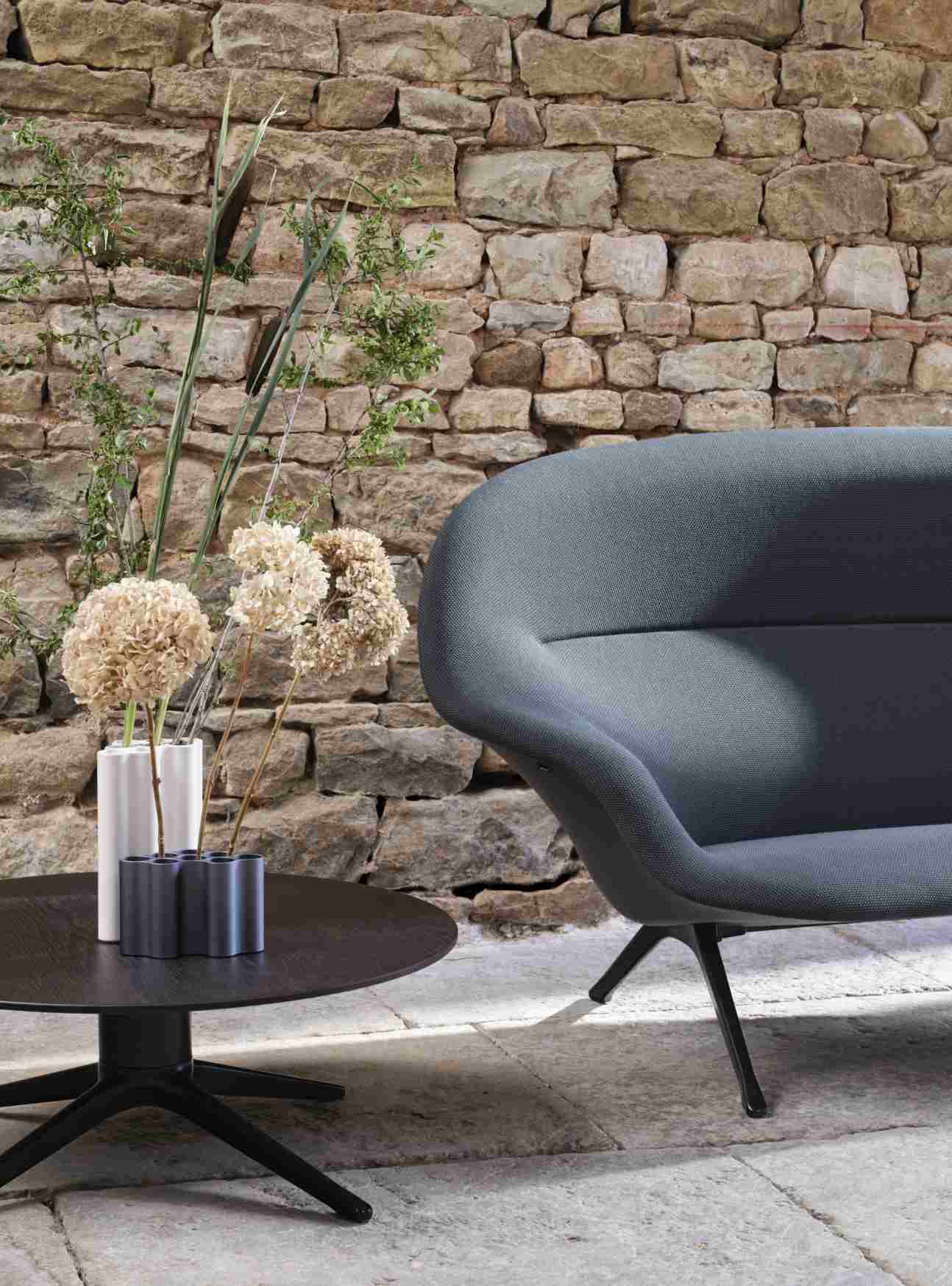 Graues Abalon Sofa von Vitra mit schwarzem Tisch und Blumenvasen vor Steinwand.