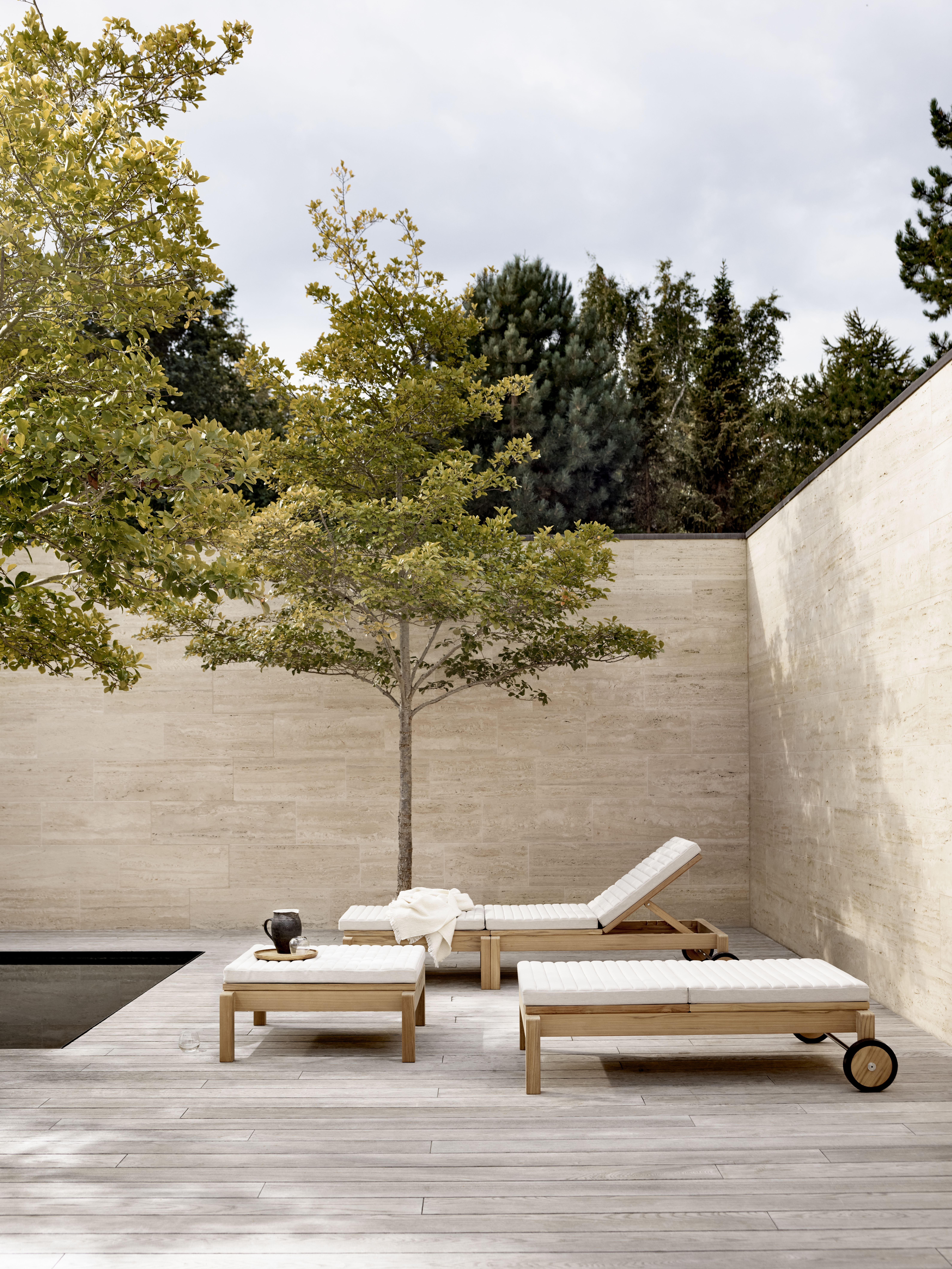 AH604 Teak Gartenliege von Carl Hansen & Søn auf Holzterrasse mit Pool und Bäumen.