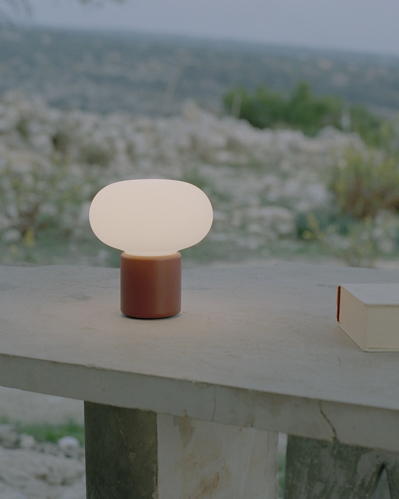 Karl-Johan Tischleuchte von New Works, Akkuleuchte mit warmem Licht auf Steintisch im Freien.
