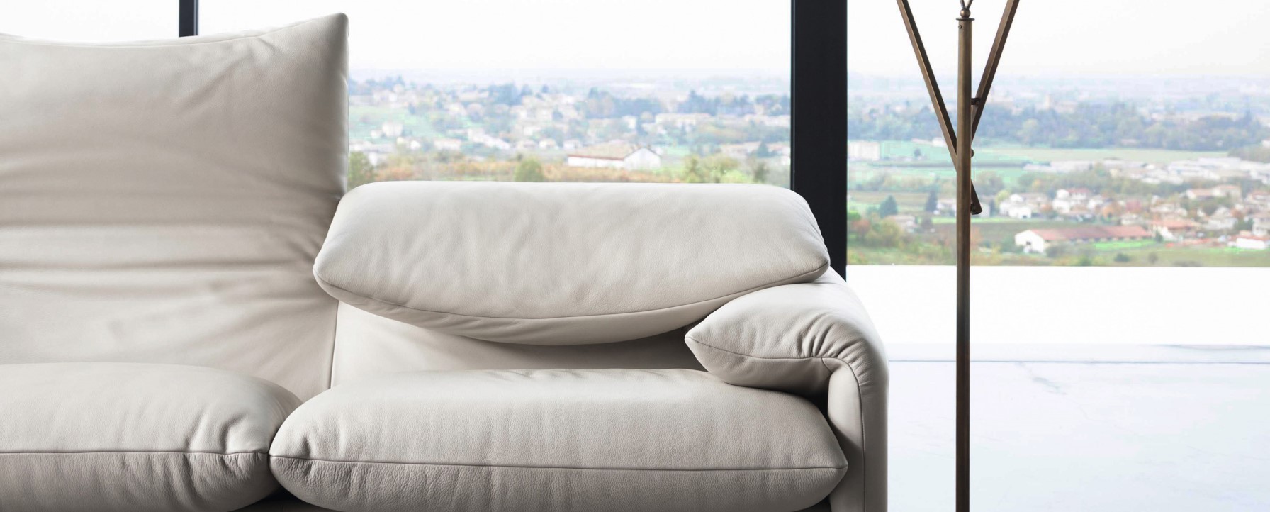 Nahaufnahme des Cassina Maralunga Sofas, ein bequemes Ledersofa in hellem Beige vor einem Panoramafenster.