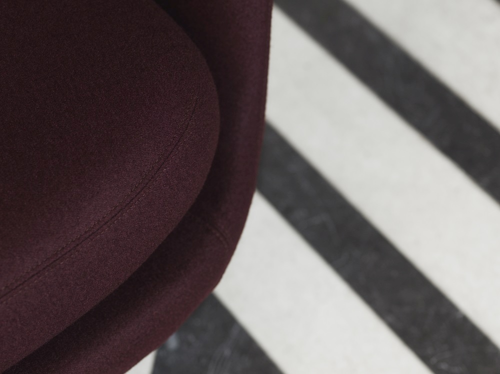 Detailaufnahme: Burgunderroter Sum Sessel von Normann Copenhagen auf einem schwarz-weiß gestreiften Teppich.