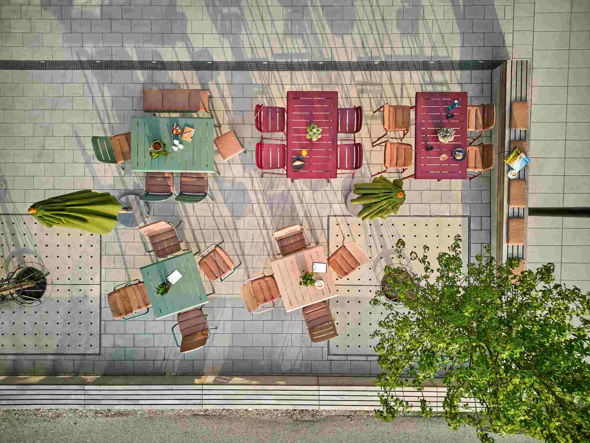 Luftaufnahme von mehreren farbigen Weishäupl Vapio Outdoor Sitzgruppen mit Tischen und Stühlen auf einer Terrasse.