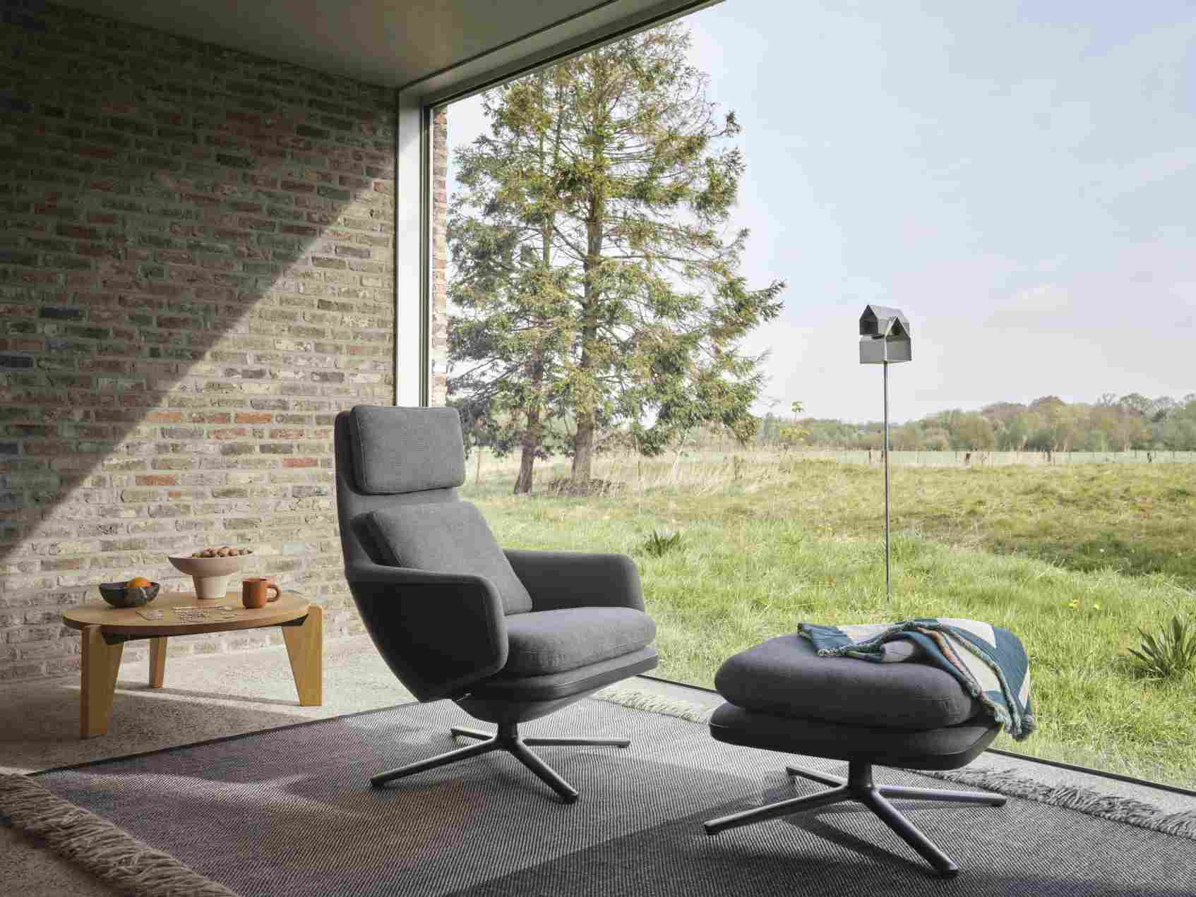 Grauer Vitra Relax Sessel mit Ottoman vor großem Fenster, komfortable Sitzgelegenheit.
