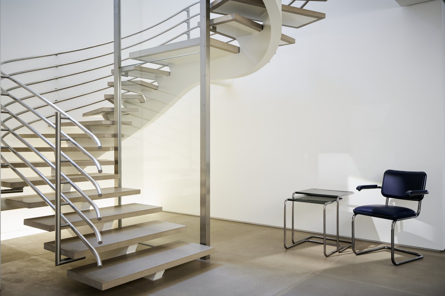 JS. Thonet S 64 P Freischwinger Stuhl in schwarzem Leder neben einem minimalistischen Treppenhaus.