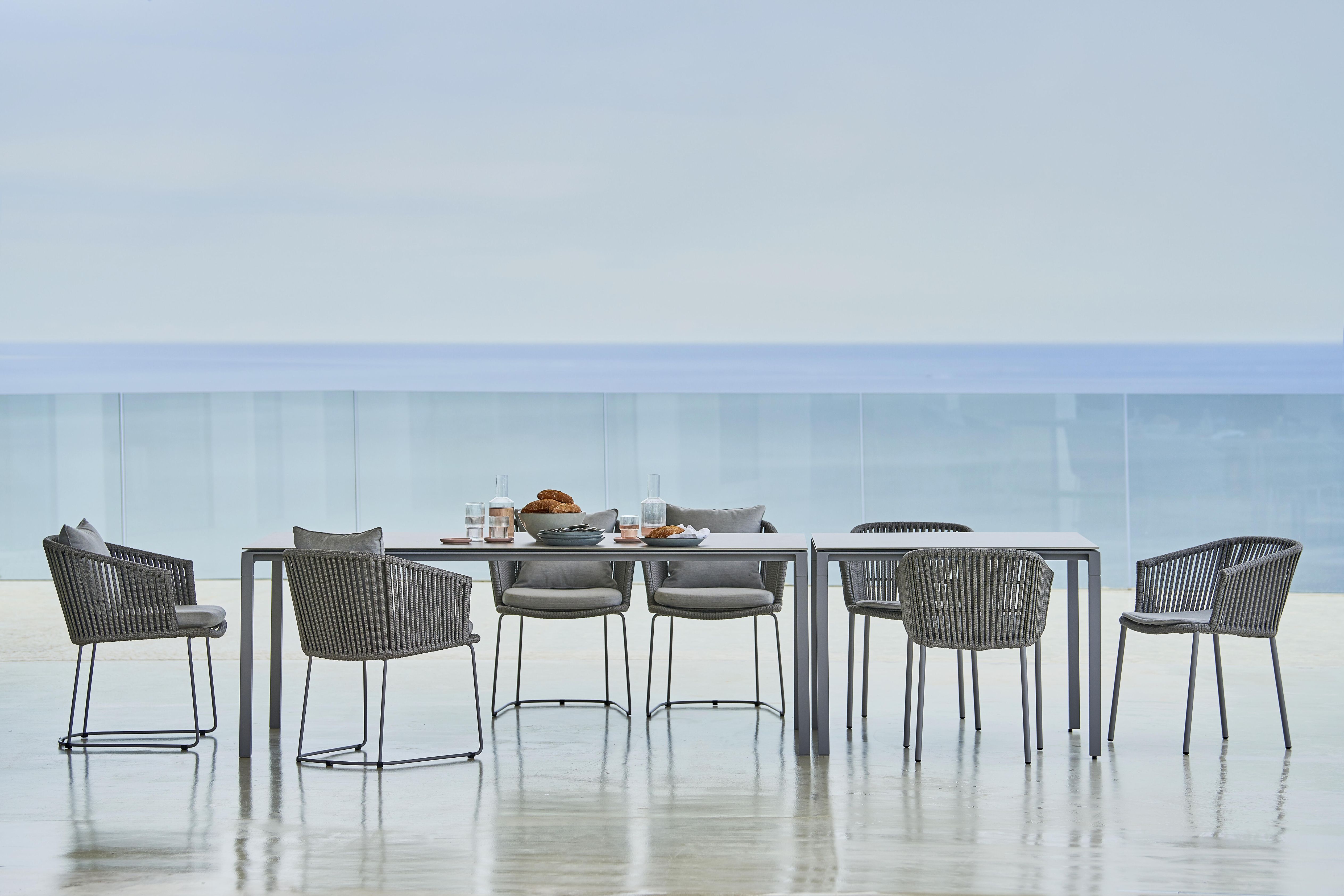 Pure Outdoor Esstisch von Cane-Line mit sechs Stühlen und grauem Seilgeflecht vor Meerblick.