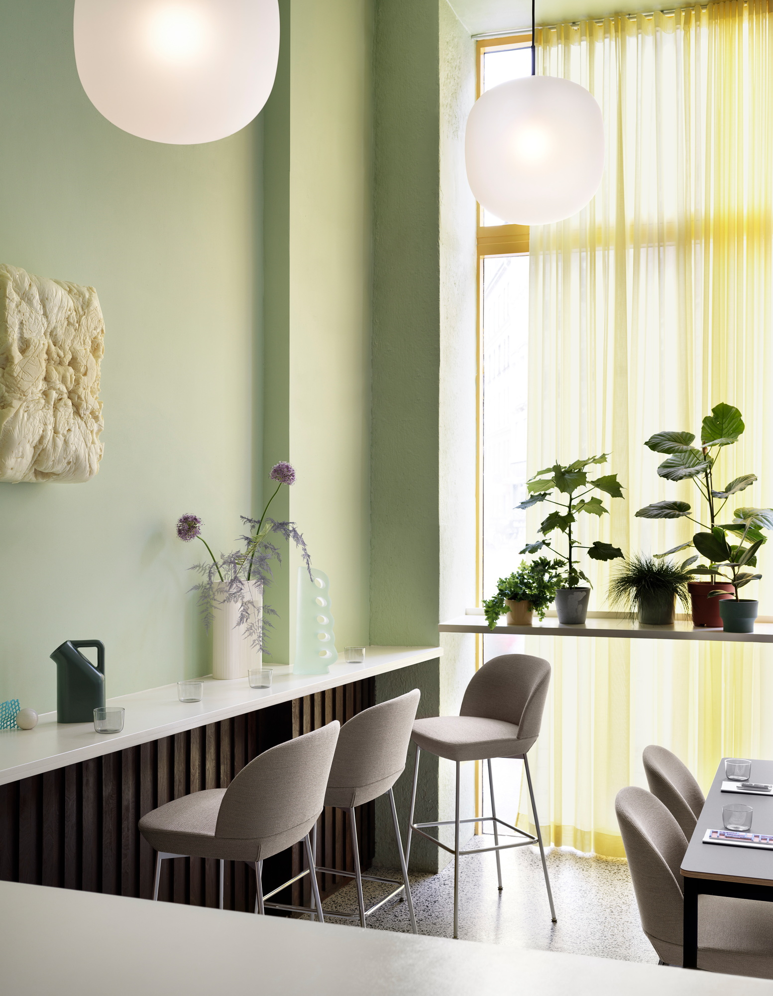 Helle, moderne Inneneinrichtung mit Rime Pendelleuchte von Muuto, graue Barhocker und Pflanzen am Fenster.