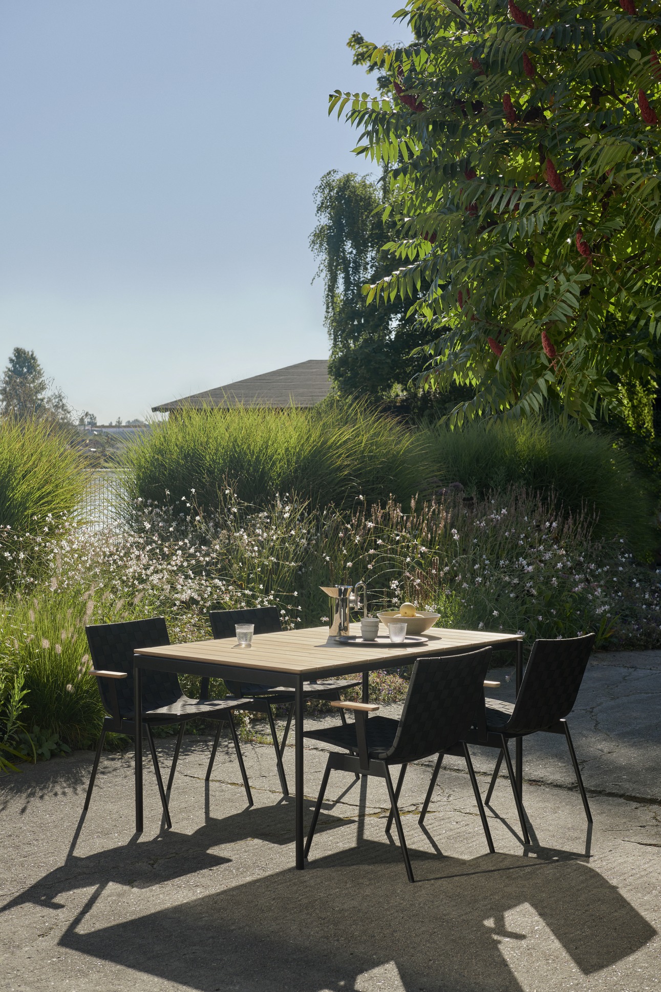 AndTradition Ville AV34 Outdoor Stuhl, schwarzes Design, mit Gartentisch und idyllischer Natur im Hintergrund.
