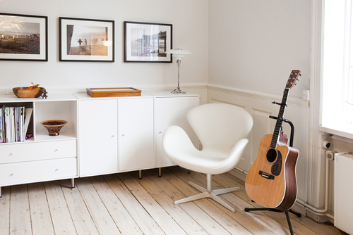 Heller Raum mit weißem Fritz Hansen Schwan Sessel, Gitarre und weißen Möbeln unter gerahmten Bildern.