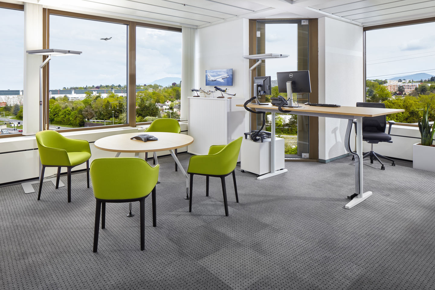 Büro mit Besprechungstisch und vier grünen Vitra Softshell Chairs mit Vierfußgestell vor großem Fenster.