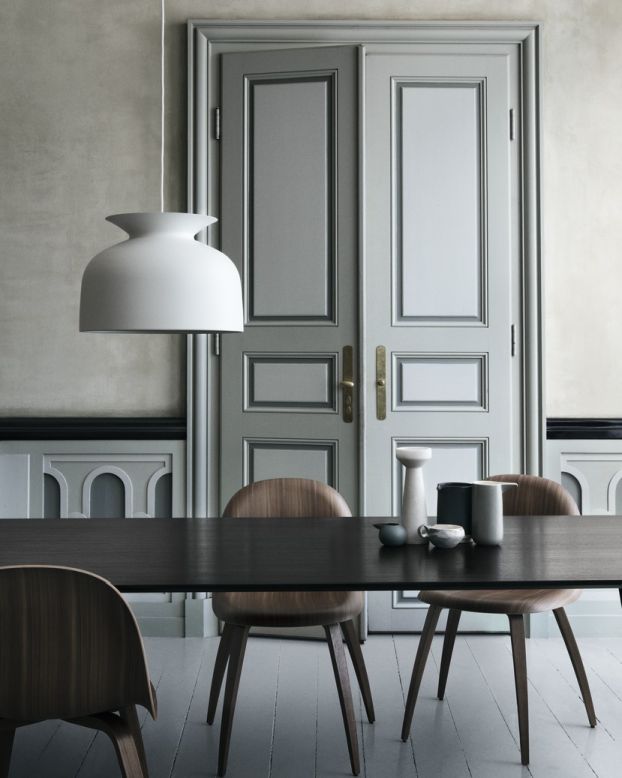 GUBI Esstisch elliptisch in dunklem Holz mit Stühlen und Pendelleuchte im Interieur.