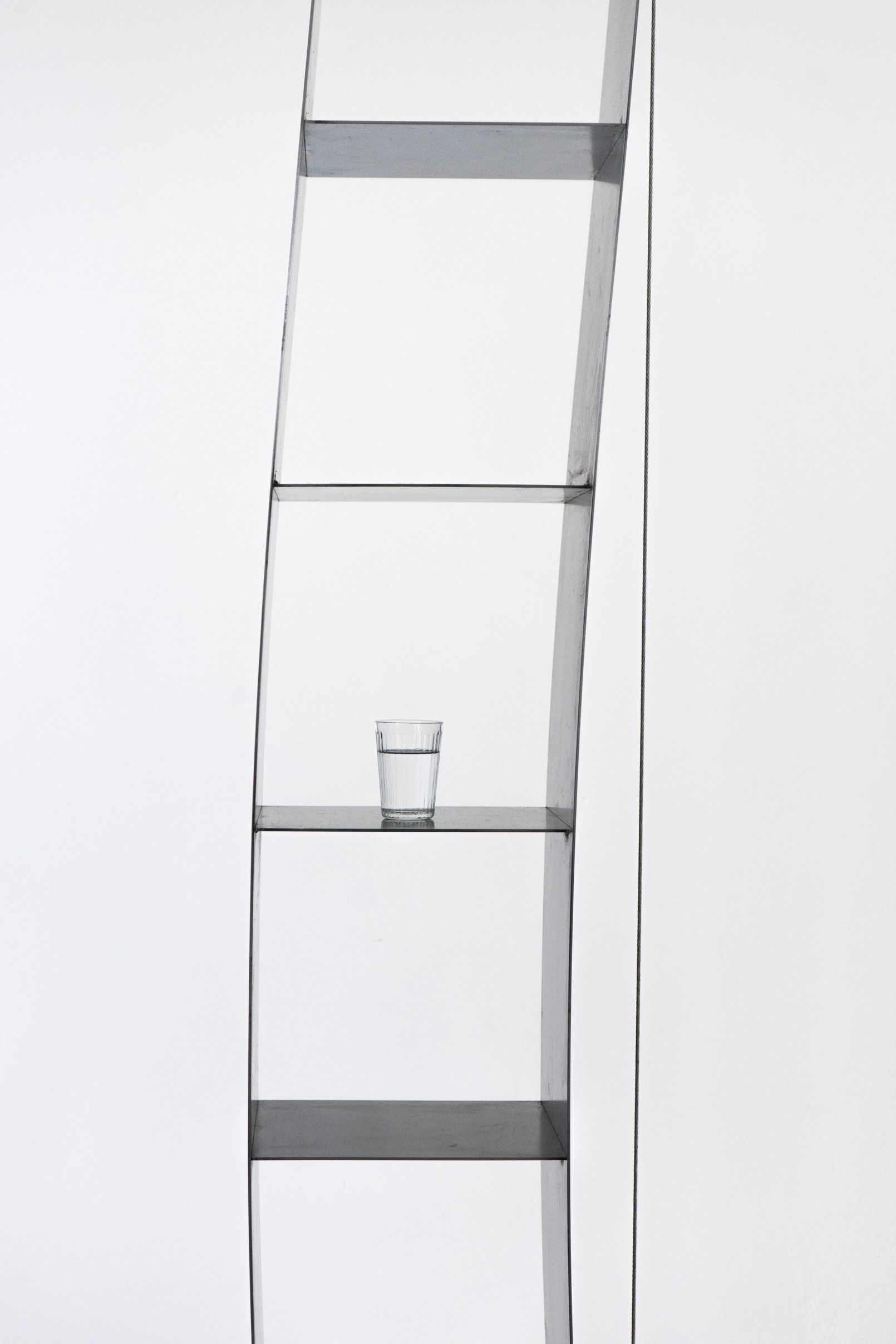 Nils Holger Moormann Gespanntes Regal vor weißer Wand mit Wasserglas auf einem der Regalböden.