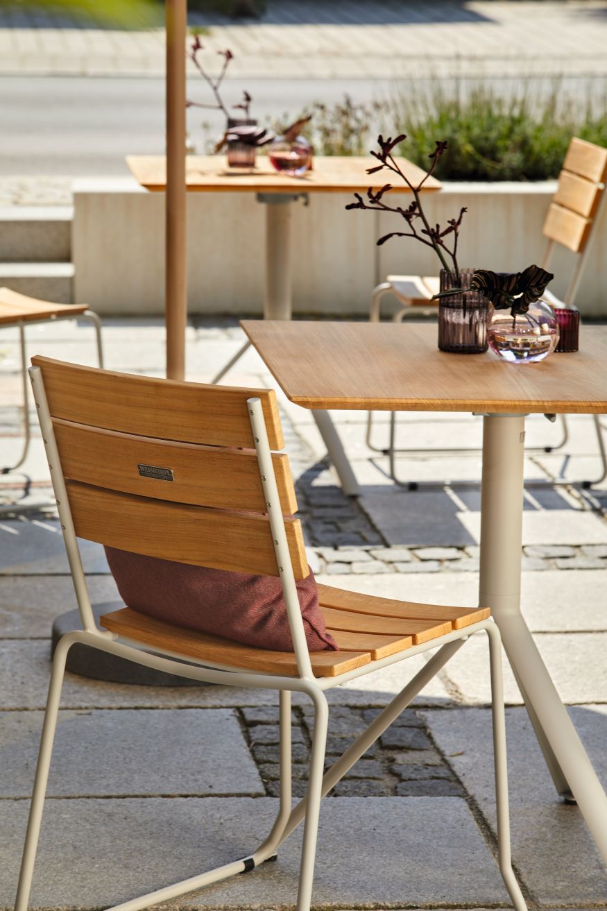 Weishäupl Balcony Klapptisch mit Teakholzplatte und Edelstahlgestell, kombiniert mit passendem Teakholzstuhl und rotem Kissen.