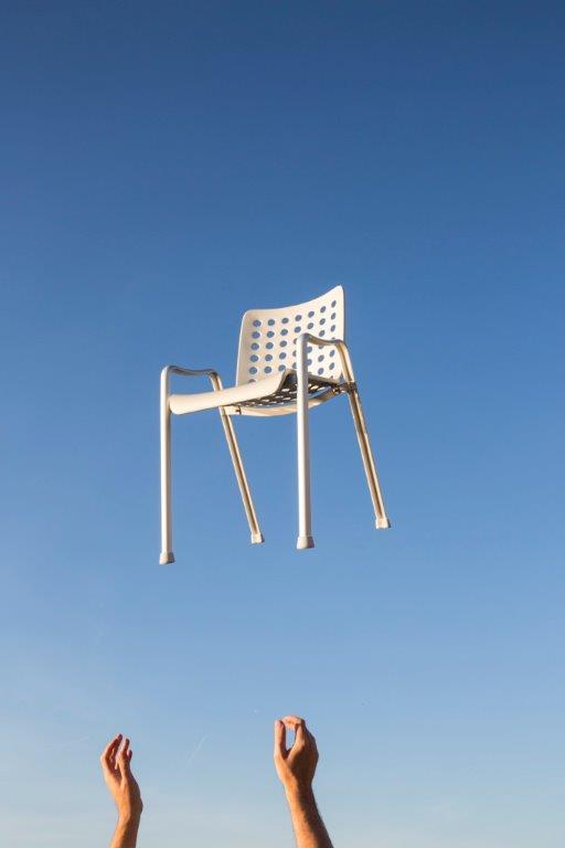 Schweben des weißen Landi Stuhls von Vitra vor blauem Himmel, Hände im Vordergrund.