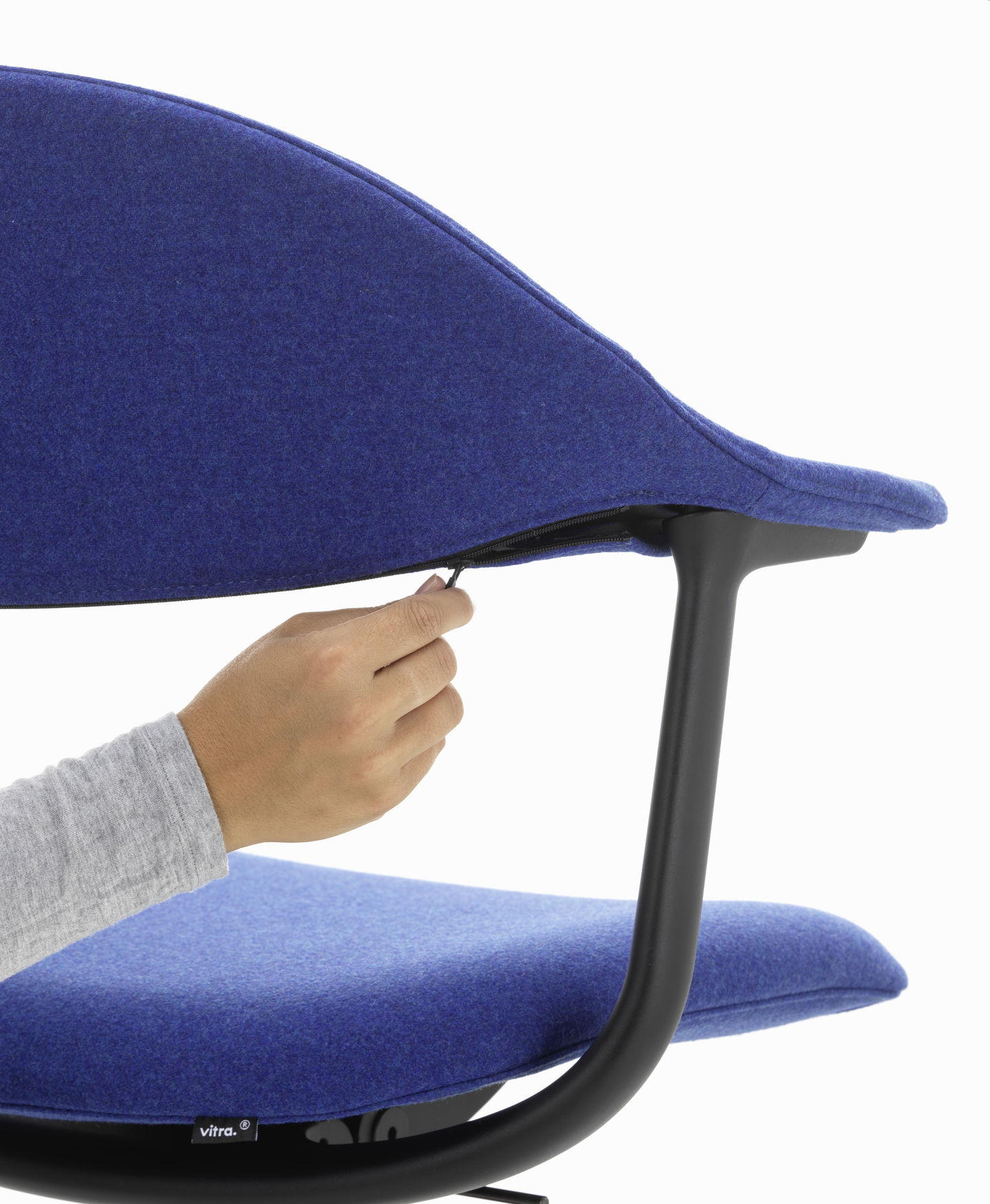 Detailaufnahme: Hand öffnet Reißverschluss am blauen Mynt Bürodrehstuhl von Vitra, ergonomischer Sitzkomfort.