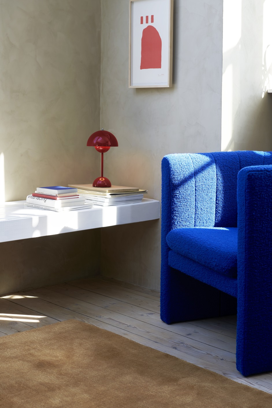 Flowerpot VP9 Tischleuchte in Vermilion Red auf Bücherstapel neben blauem Sessel.