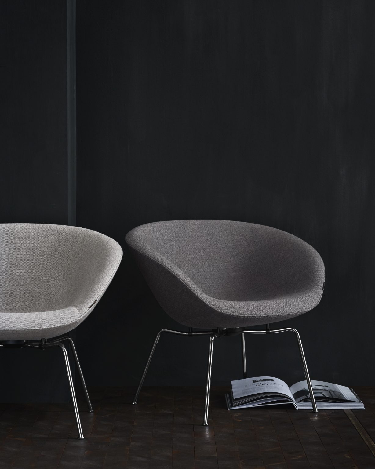 Zwei graue Fritz Hansen Pot Sessel mit Chrombeinen vor dunkler Wand, moderner Lounge Sessel.