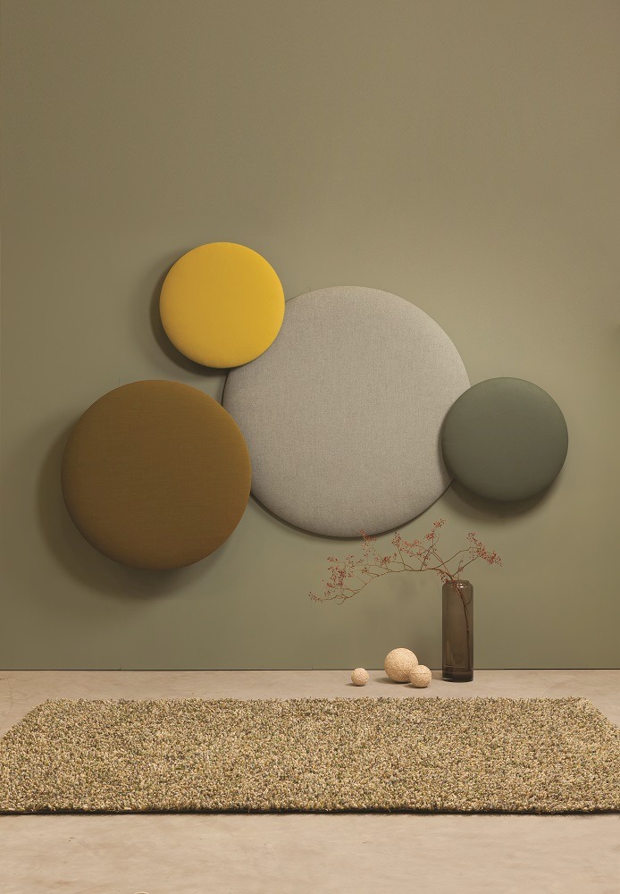 Wandbild: Cascando Pillow Round Akustikelemente in Gelb, Grau, Braun und Grün an grüner Wand.
