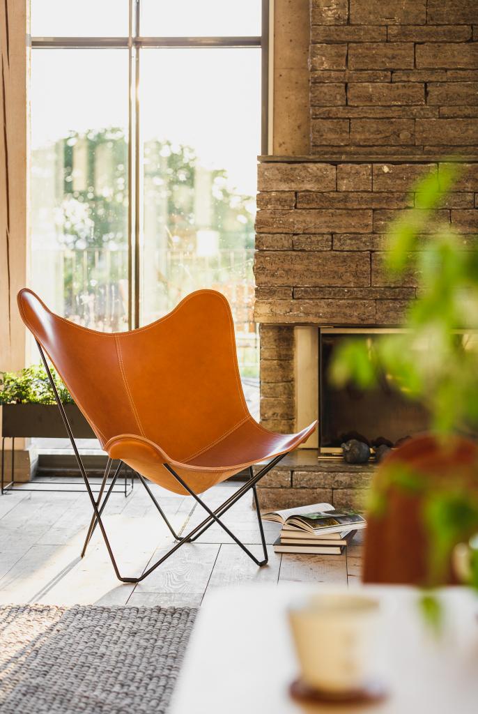 Pampa Butterfly Chair Sessel aus braunem Leder mit schwarzem Metallgestell vor Fenster.