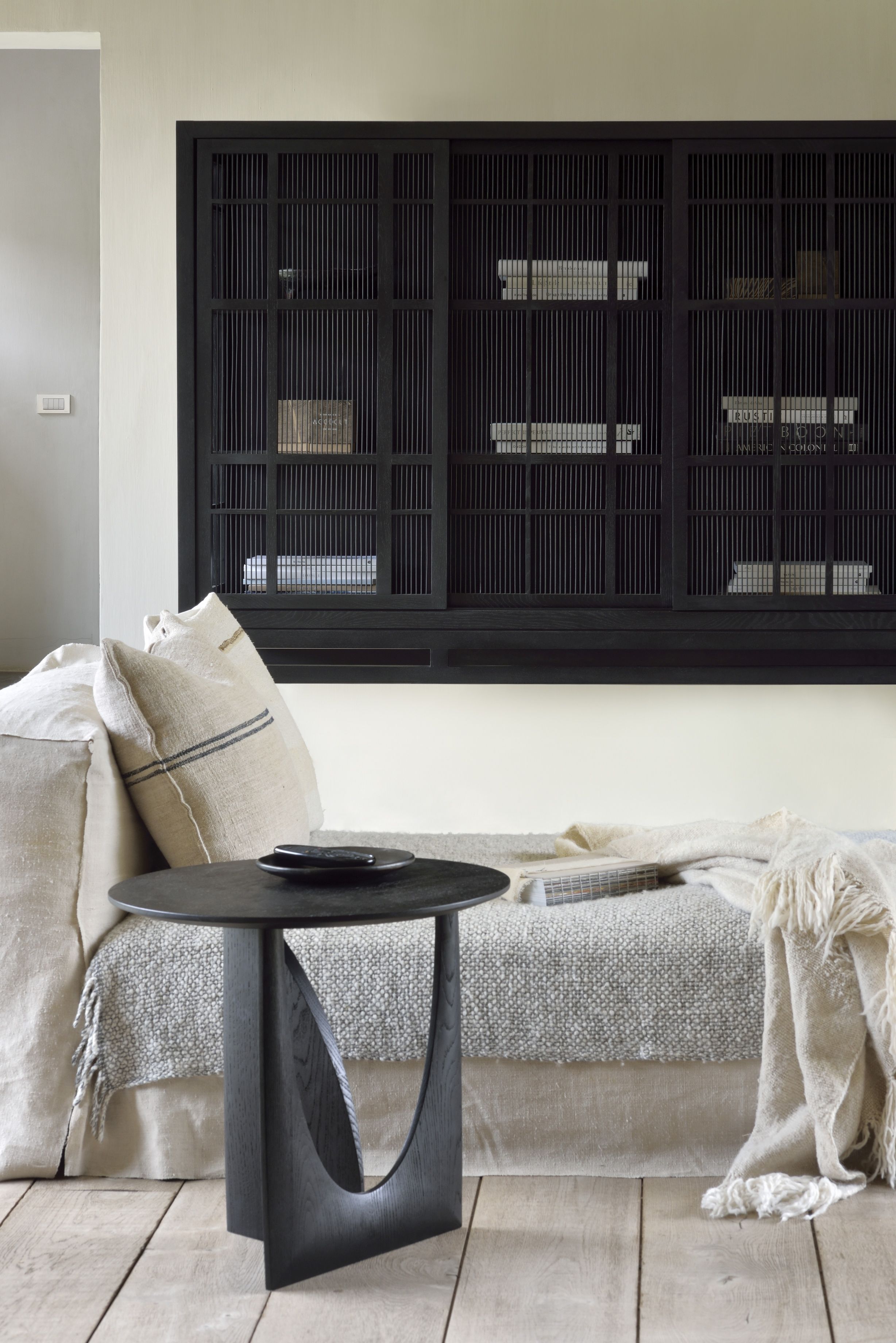 Geometric Beistelltisch aus Teakholz von Ethnicraft neben einem Sofa mit Kissen und Decke.