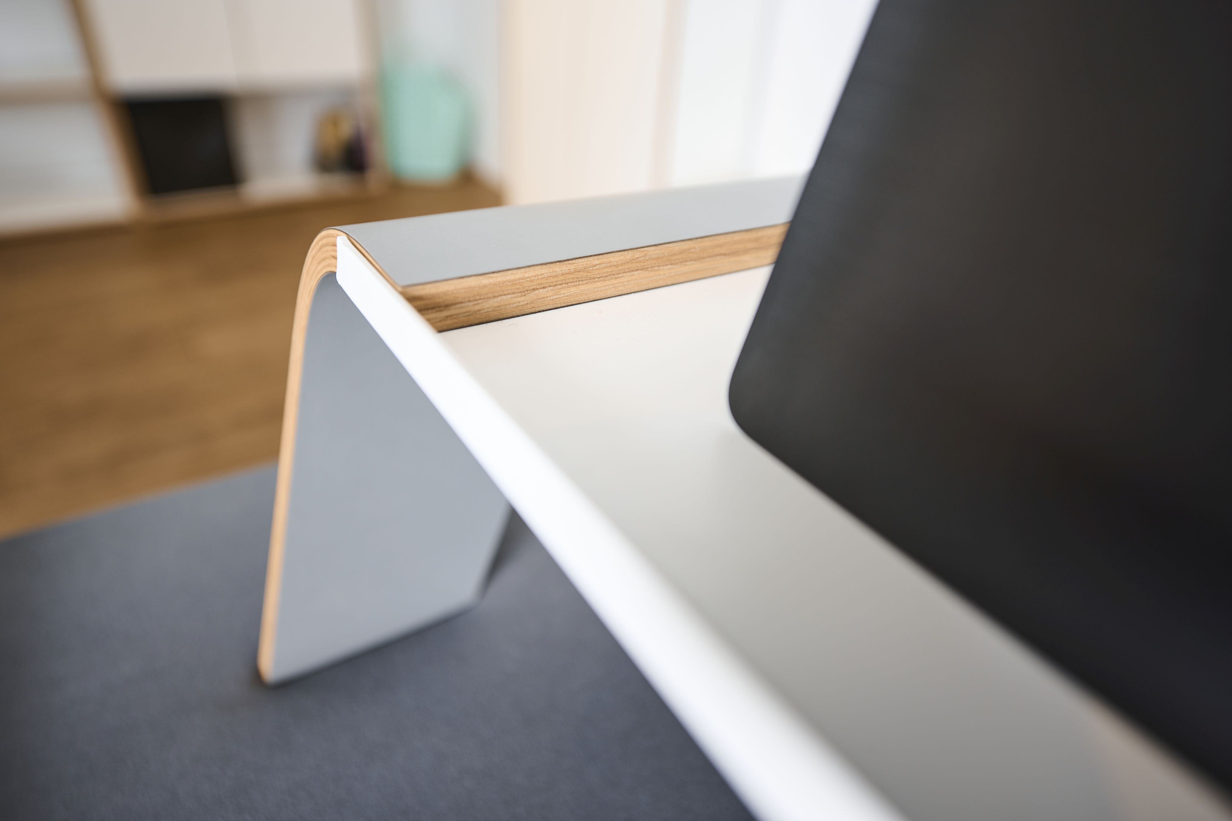 Detailaufnahme des Tojo Notebook-Tabletts: Modernes, weißes Beistelltisch-Design mit Laptop auf grauem Untergrund.