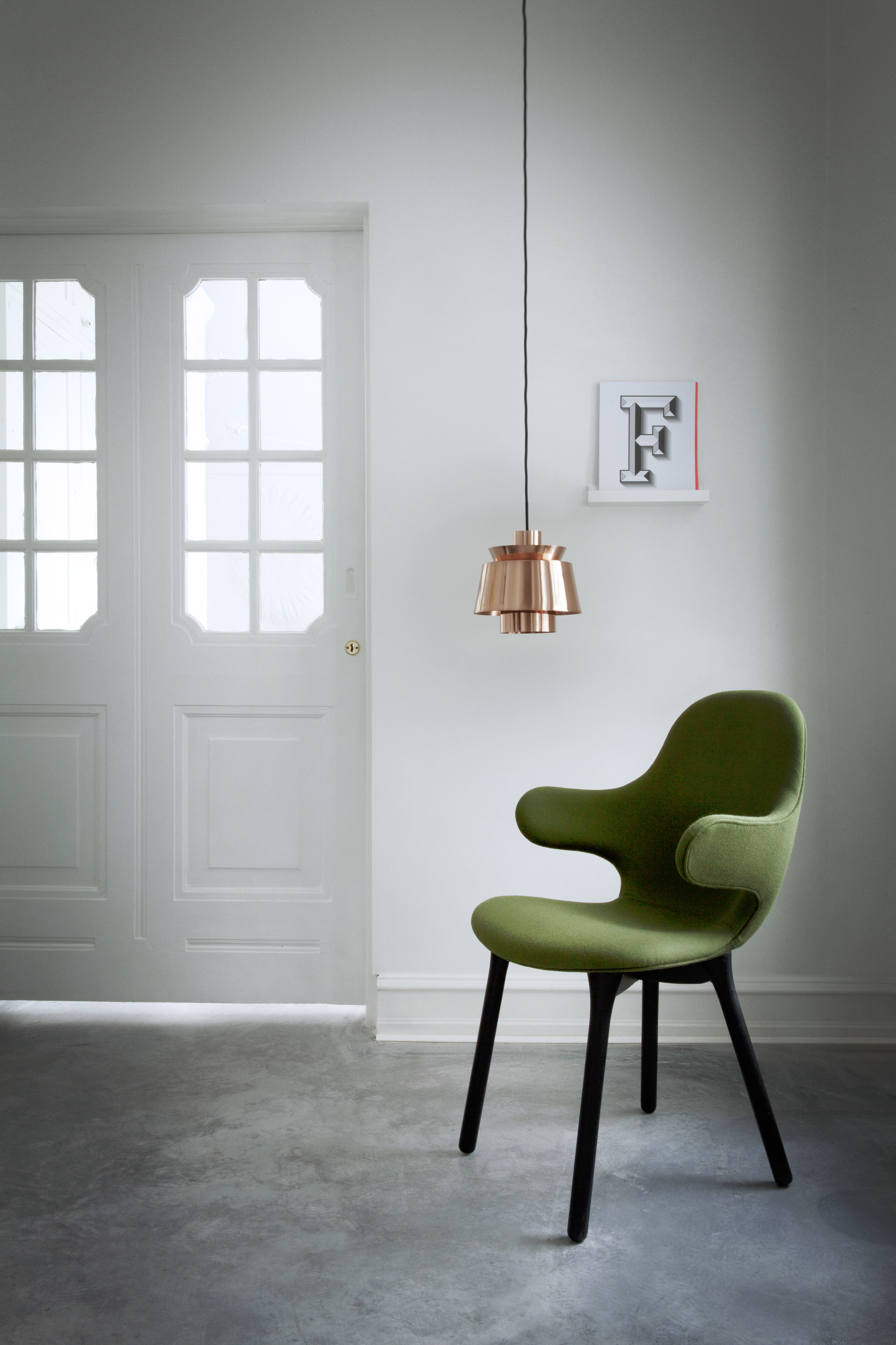 AndTradition Catch Chair JH1 Stuhl in Grün mit schwarzen Beinen vor weißer Tür und Lampe.