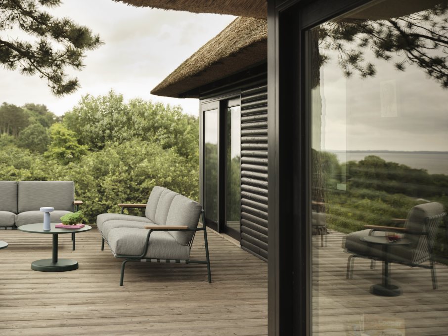 Muuto Settle Outdoor Sofa, grauer 2-Sitzer mit Holzelementen und passendem Gartentisch auf Holzterrasse.