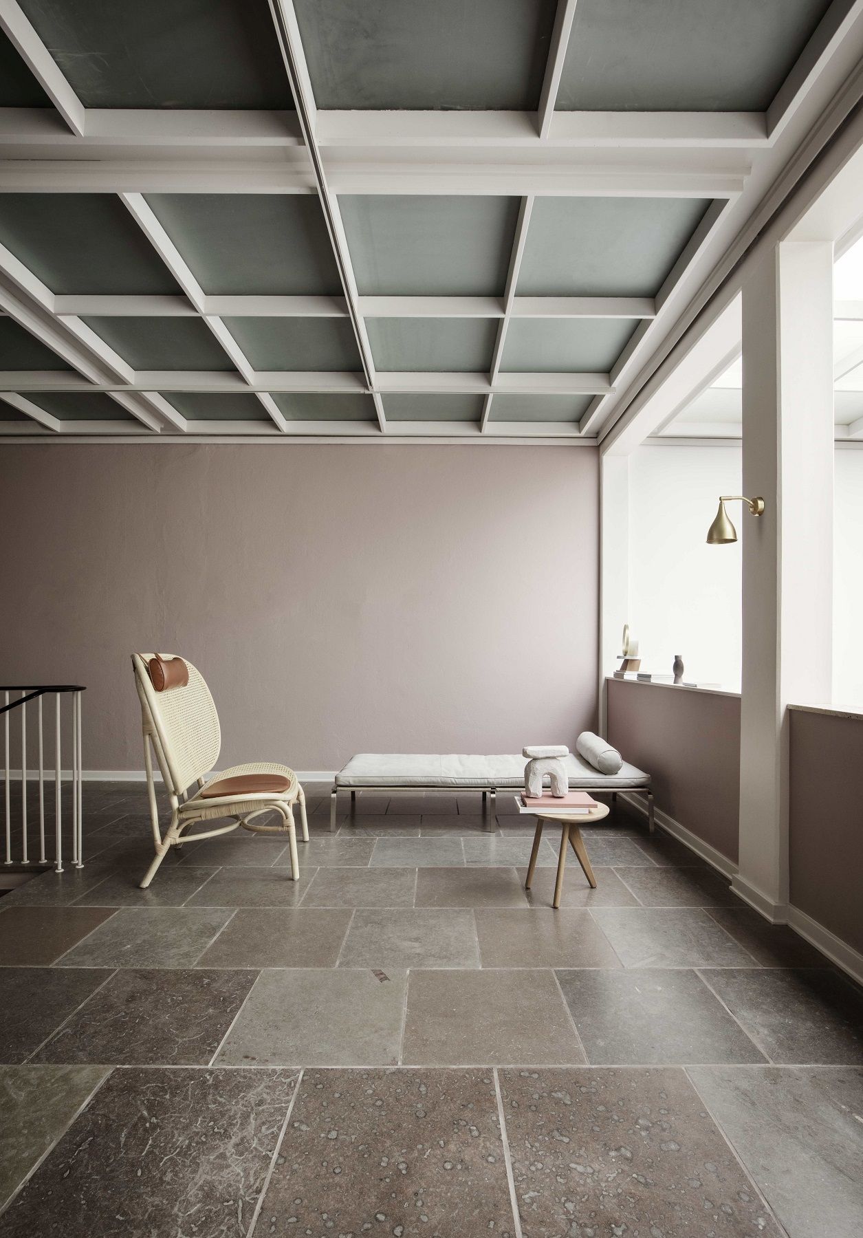 Innenaufnahme eines Raumes mit NORR11 Man Daybed Tagesbett, Rattansessel und kleinem Beistelltisch auf Steinfußboden.