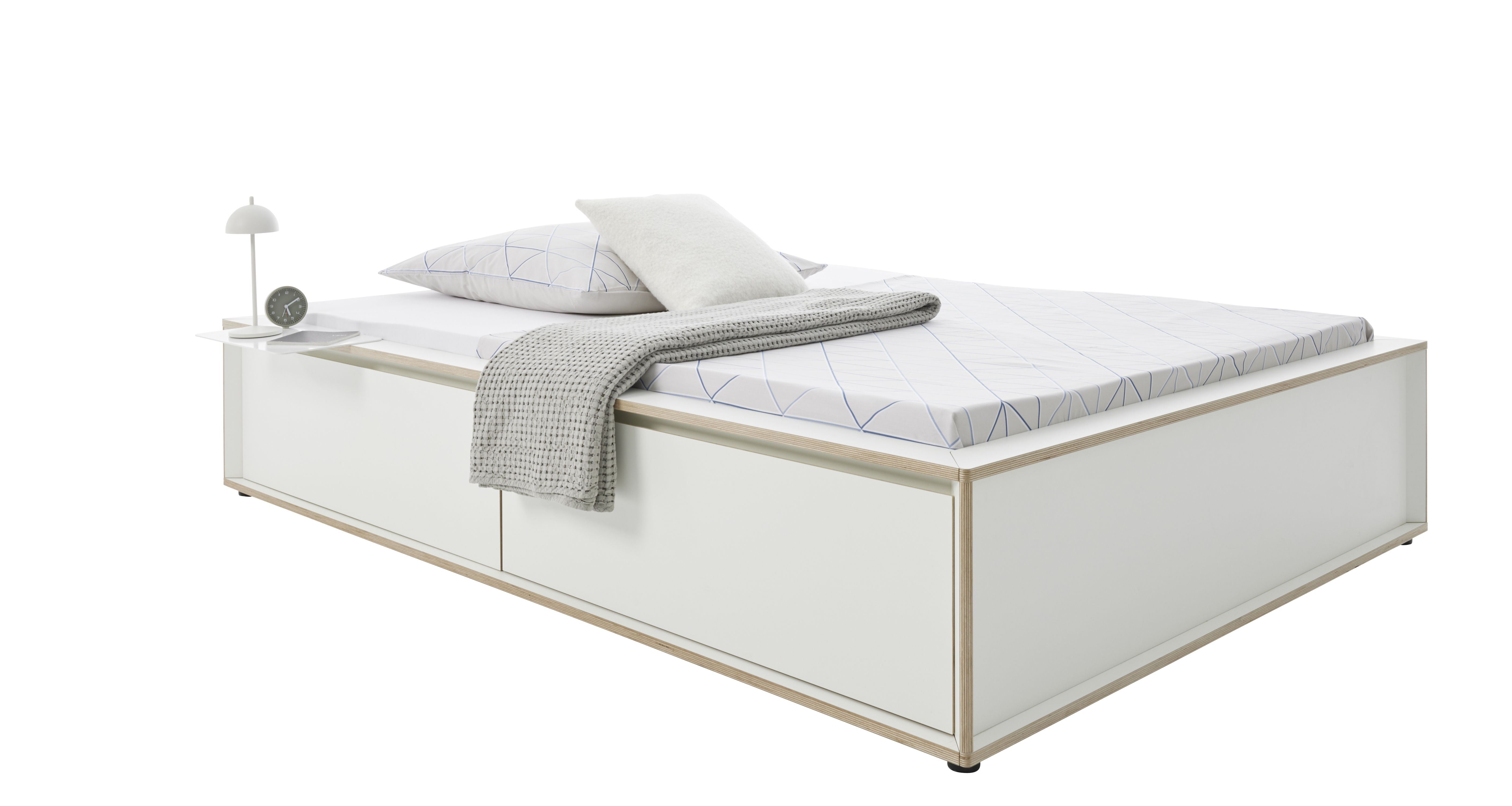 Spaze Bett von Müller Möbelwerkstätten, weißes Plattformbett mit Schubladen, Nachttisch, Lampe, Kissen und Decke.