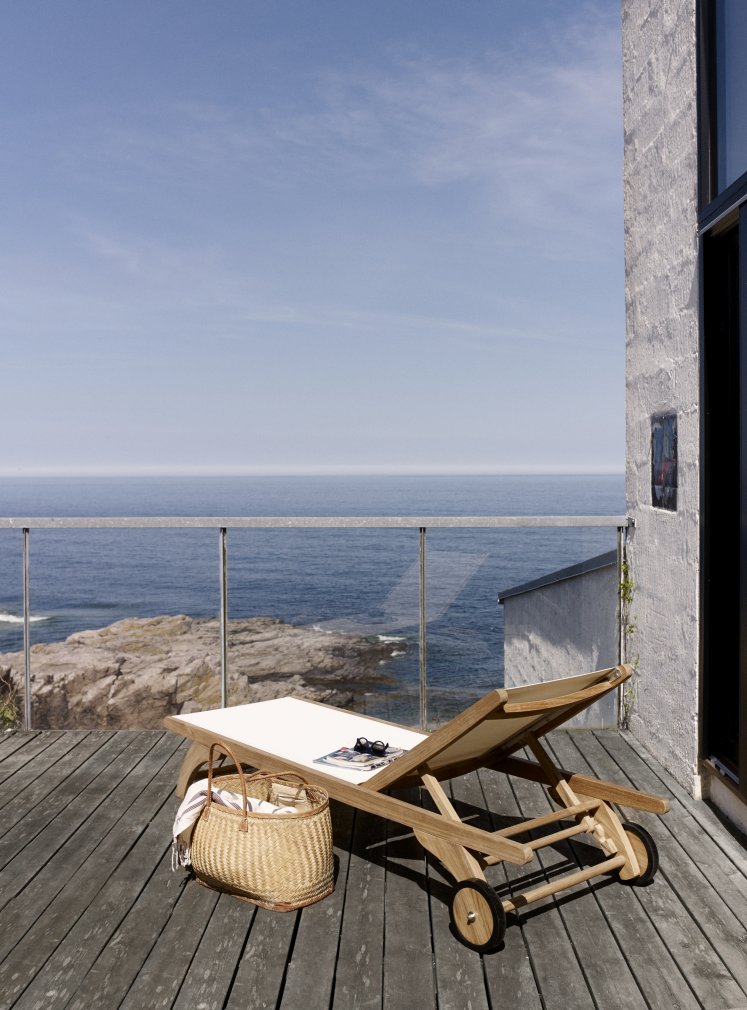 Columbus Sonnenliege von Skagerak auf Holzterrasse mit Meerblick, Korb und Accessoires. Outdoor Möbel.