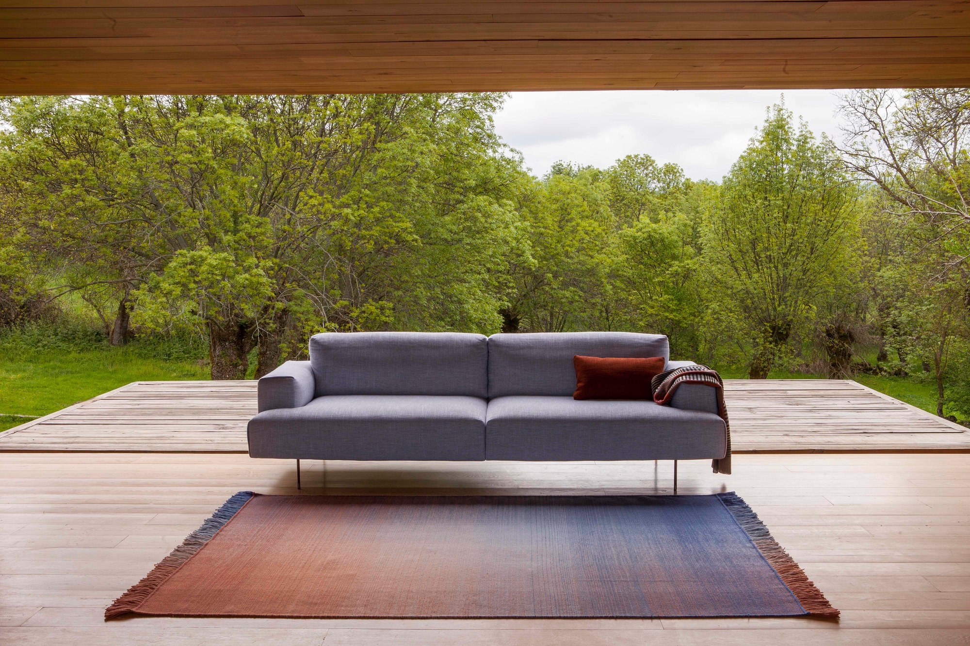 Nanimarquina Shade Teppich im Innenraum mit Farbverlauf von Blau zu Terrakotta vor Sofa.