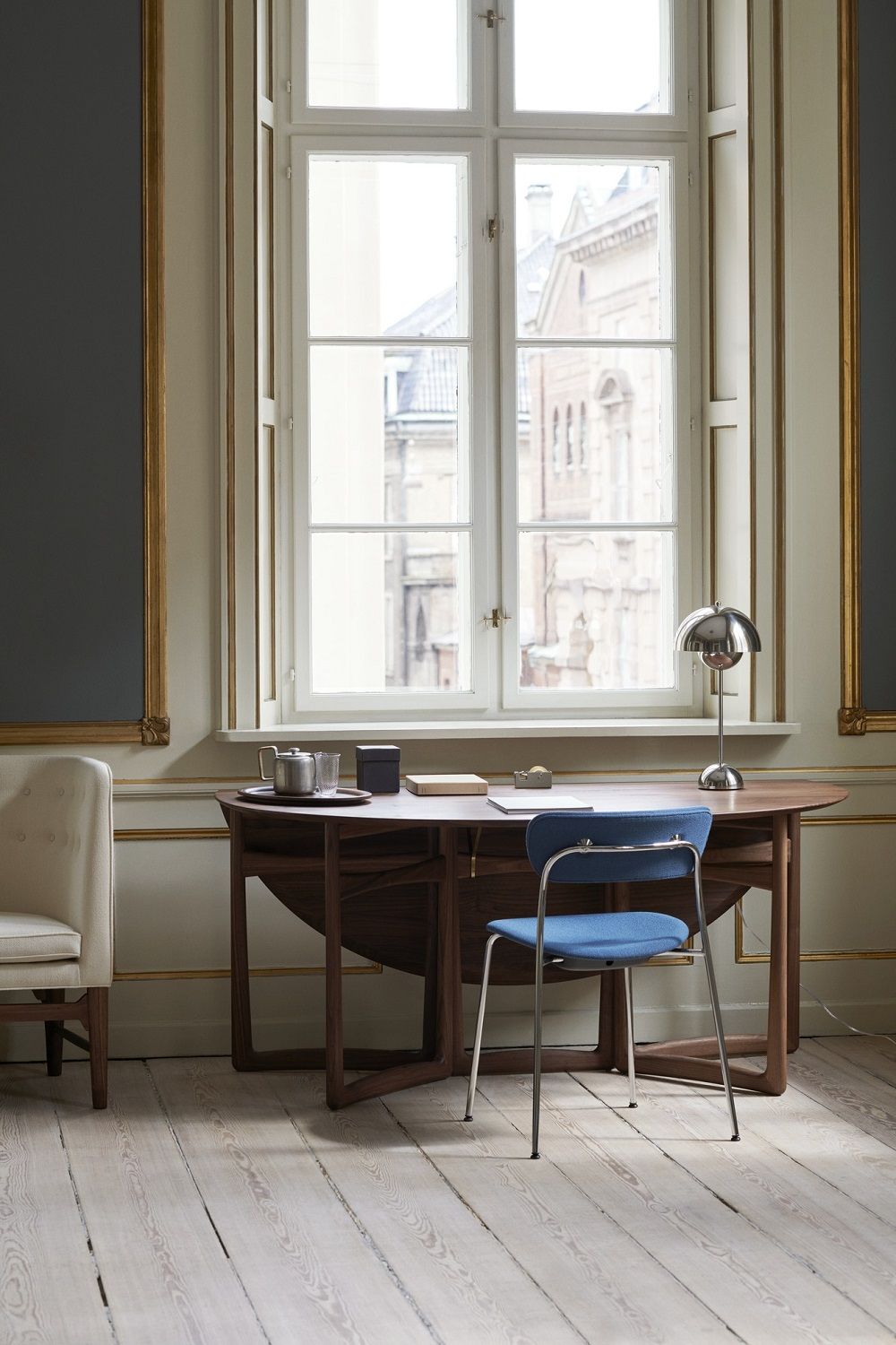 AndTradition Drop Leaf HM6 Tisch aus Holz mit blauem Stuhl vor Fenster.