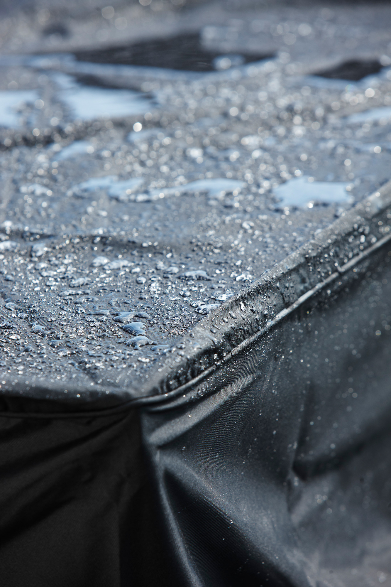 Detailaufnahme einer schwarzen Cane-Line Schutzhülle für Gartenmöbel, bedeckt mit Wassertropfen, die ihre Wasserdichtigkeit demonstrieren.