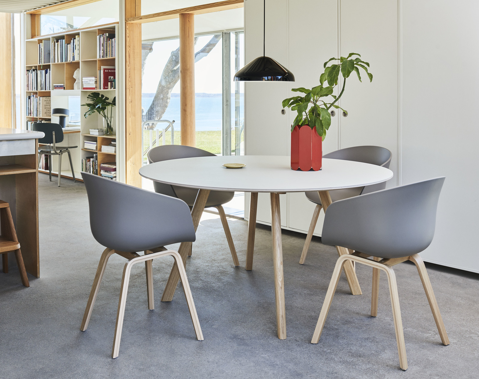 Weißer runder Esstisch mit vier grauen Stühlen und rotem Blumentopf in modernem Esszimmer.